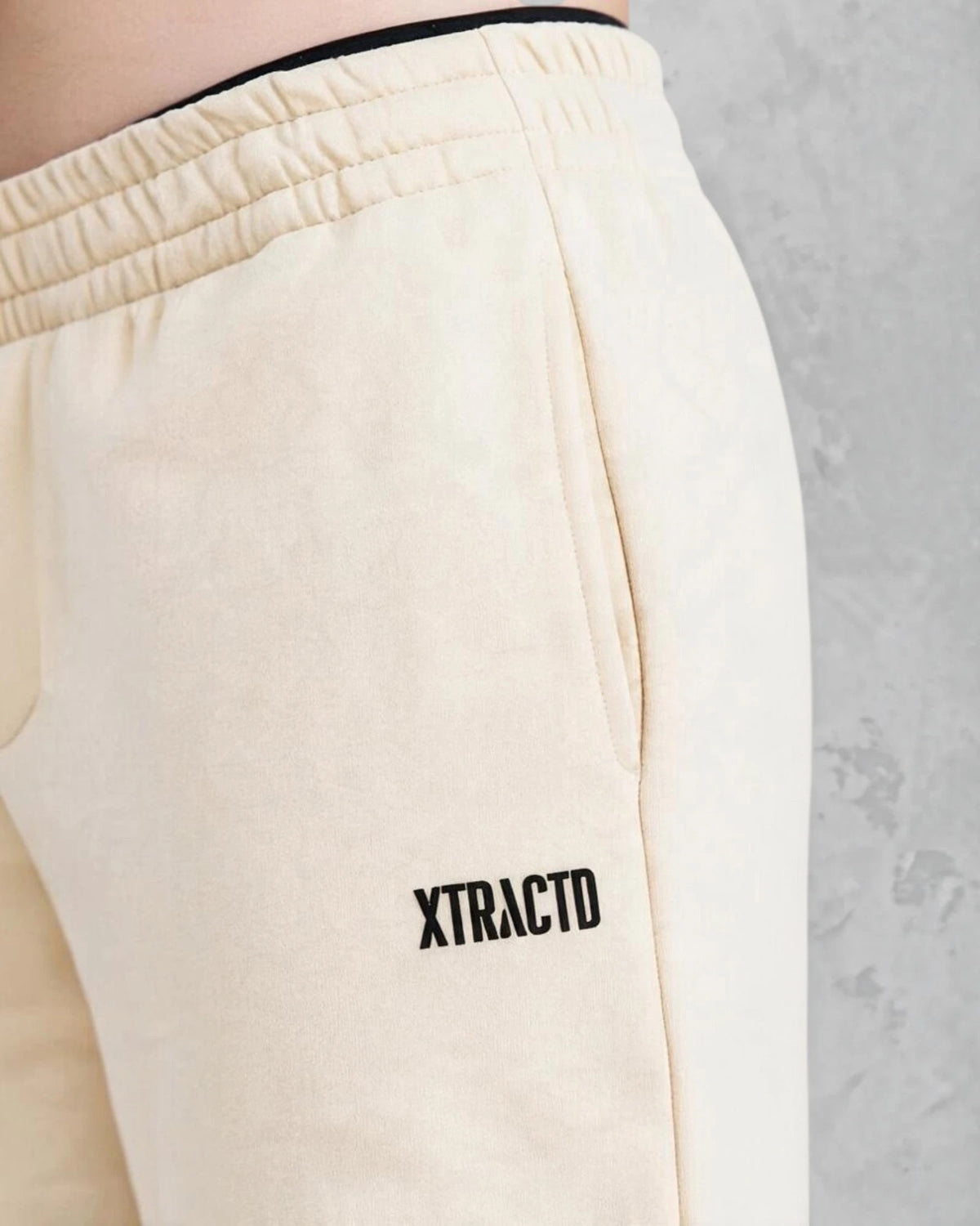Detail der XTRACTD Sweatpants Oat Milk mit schwarzem Logo und elastischem Bund
