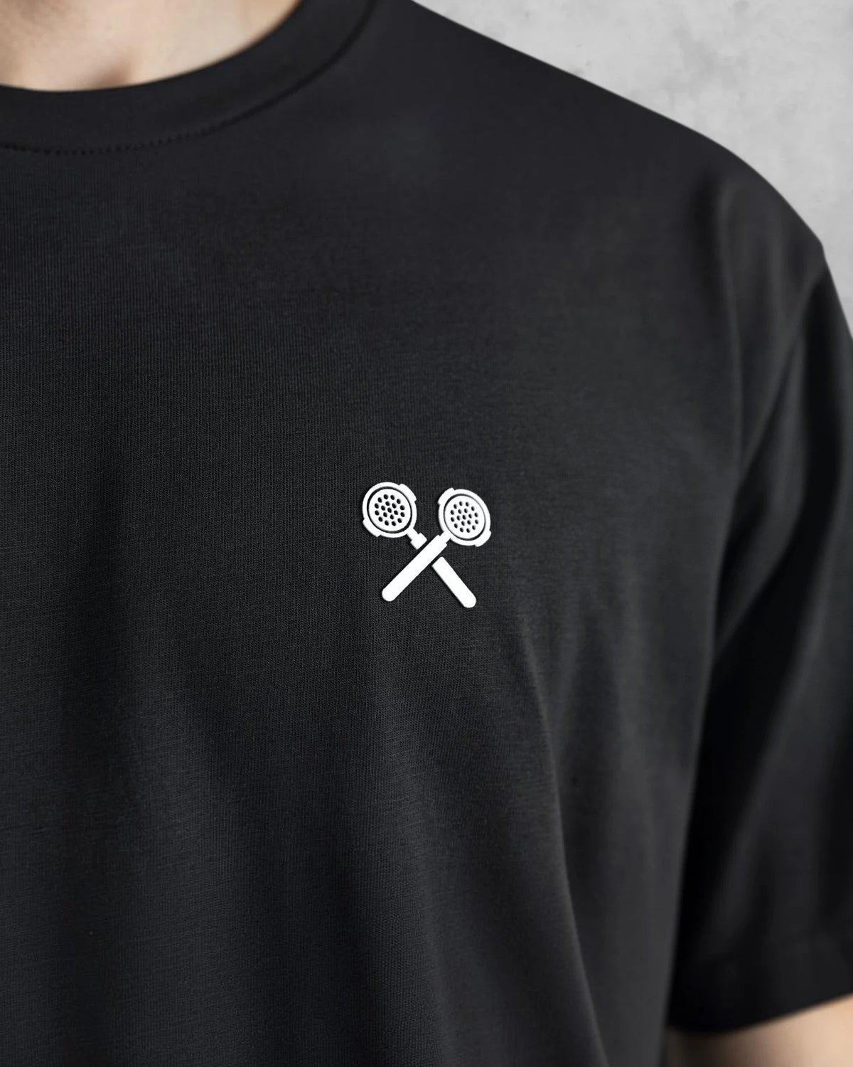 Nahaufnahme des weißen gekreuzten Siebträger-Logos auf dem schwarzen XTRACTD T-Shirt